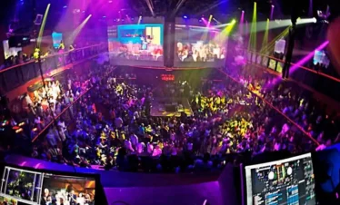 A crowded nightclub on your Punta Cana trip, filled with people dancing under vibrant neon lights. The photo, taken from the DJ booth, overlooks the energetic dance floor and two upper balconies—an unforgettable highlight among Punta Cana excursions.