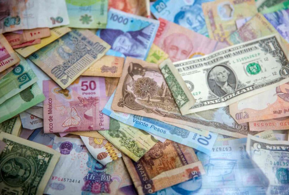 A scattered assortment of colorful banknotes from various countries, perfect for illustrating the best ways to take money abroad, with Mexican pesos, US dollars, and other currencies overlapping in a disorganized pile.