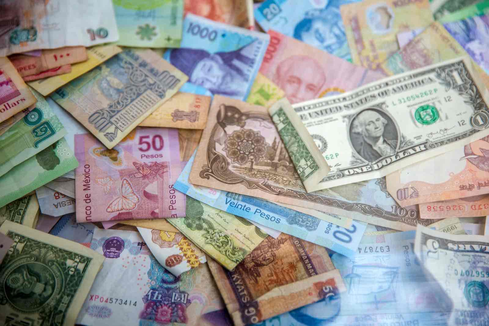 A scattered assortment of colorful banknotes from various countries, perfect for illustrating the best ways to take money abroad, with Mexican pesos, US dollars, and other currencies overlapping in a disorganized pile.