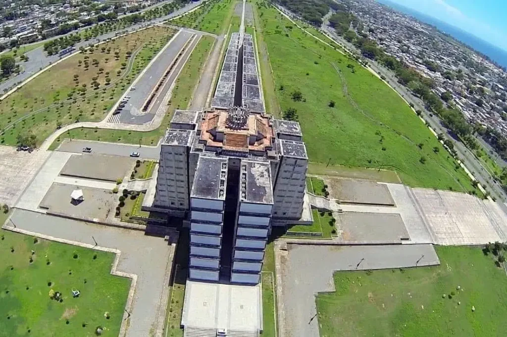 Aerial view of a large, rectangular concrete building with tiered sections and a cross-shaped layout, surrounded by wide paved walkways and vast green lawns—an impressive urban scene perfect to admire before or after your Punta Cana excursions.