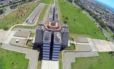 Aerial view of a large, rectangular concrete building with tiered sections and a cross-shaped layout, surrounded by wide paved walkways and vast green lawns—an impressive urban scene perfect to admire before or after your Punta Cana excursions.