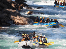 Three inflatable rafts, each carrying groups of people with helmets and life jackets, navigate through white-water rapids. The river is turbulent as the group in the foreground paddles together on exciting tours en Punta Cana.