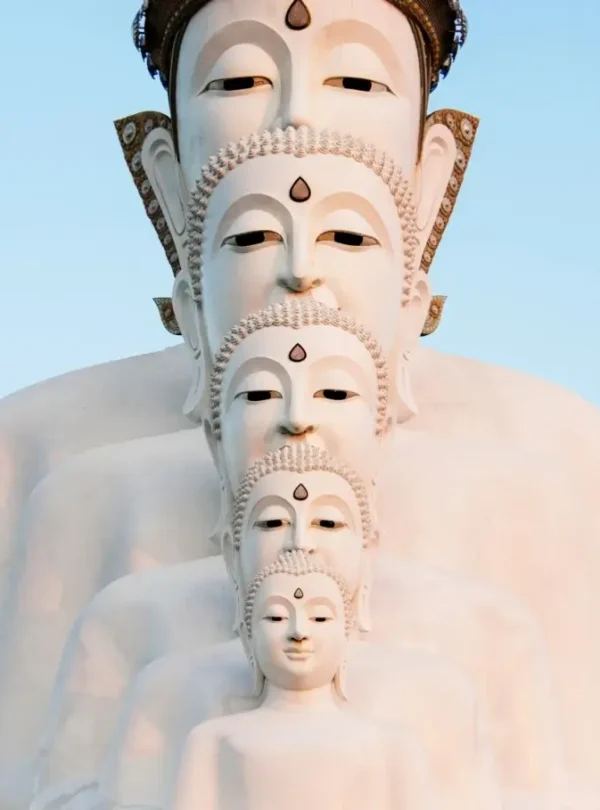 A row of five large white Buddha statues, each positioned in front of the other, creates a layered effect. Perfect for those seeking tranquility after the best tours, their serene expressions and ornate details stand out against a clear blue sky.