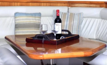 A polished wooden table with a dark tray holding a bottle of red wine and two glasses sits before a white, cushioned corner sofa—inviting you to unwind after memorable Punta Cana tours or excursions. Striped pillows in blue, beige, and gray add a serene touch.