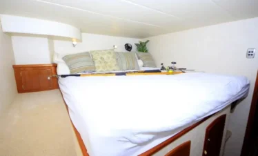 A cozy, compact bedroom features a neatly made bed with white bedding and patterned pillows. Fishing rods rest on the bed, evoking adventure—perfect for relaxing after tours in Punta Cana. Wooden cabinets and beige carpeting suggest the room is inside a boat or RV.