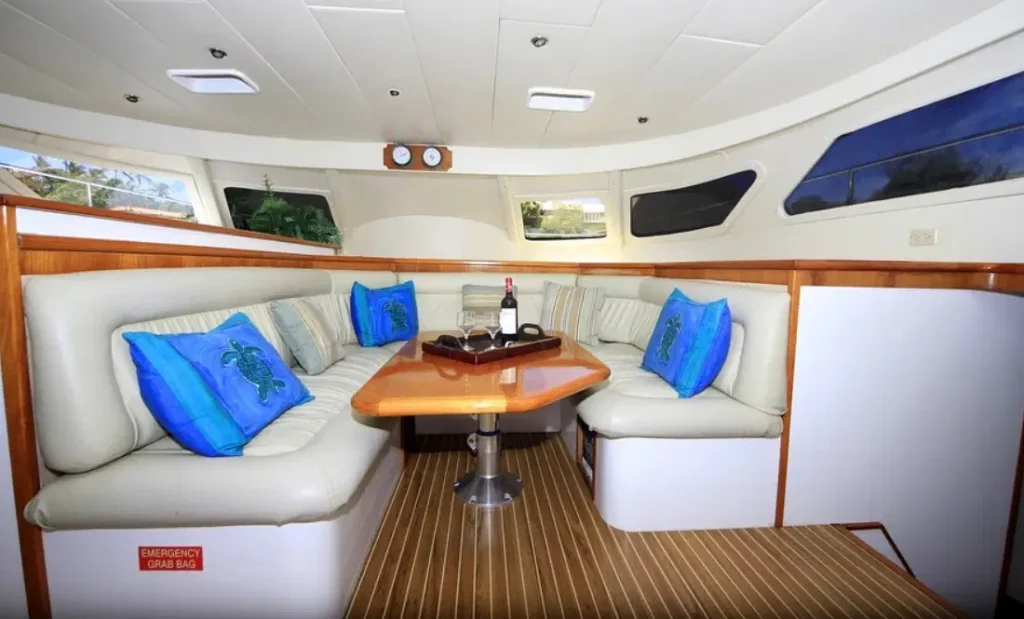 A modern yacht’s interior lounge with cream leather seating around a wooden table sets the mood for unforgettable Punta Cana excursions. Blue turtle pillows, wine glasses, and scenic views complete this perfect spot for your tours in Punta Cana.