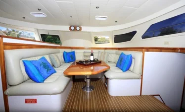 A modern yacht’s interior lounge with cream leather seating around a wooden table sets the mood for unforgettable Punta Cana excursions. Blue turtle pillows, wine glasses, and scenic views complete this perfect spot for your tours in Punta Cana.
