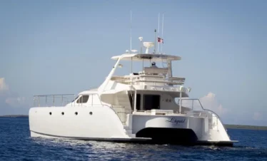 A large white catamaran yacht named "Liquid" floats on calm blue water under a clear sky, ready for unforgettable punta cana tours. The yacht features multiple decks, antennas, railings, wide hulls, and an open aft deck with a small flag on top.