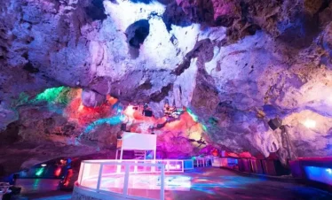 A vibrant nightclub set inside a natural cave, Imagine Punta Cana boasts colorful lights illuminating rocky ceilings and walls. A white DJ booth, reflective floors, and unique seating areas showcase the best of Punta Cana nightlife.