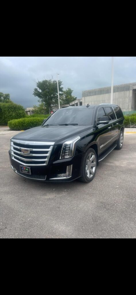 A shiny black Cadillac Escalade SUV is parked in an outdoor lot, ready for a VIP transfer. The vehicle features chrome detailing, tinted windows, and large silver wheels. Trees, a building, and a cloudy sky frame this Punta Cana arrival scene.