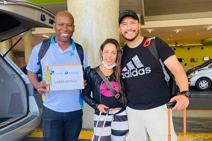 Three people stand smiling outside near parked vehicles. The man on the left holds a "Lasso Nataly" sign. They could be ready for one of the exciting tours in Punta Cana, perfect for any Punta Cana trip adventure.
